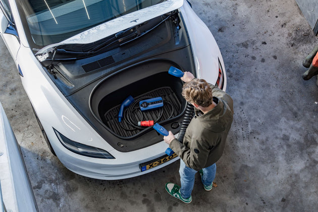 Man lifting a blue Voldt EV charging cable out of the front trunk of a white Tesla